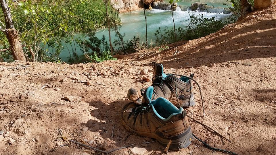 Worn hiking boots resting on a dusty trail above turquoise Havasu Creek